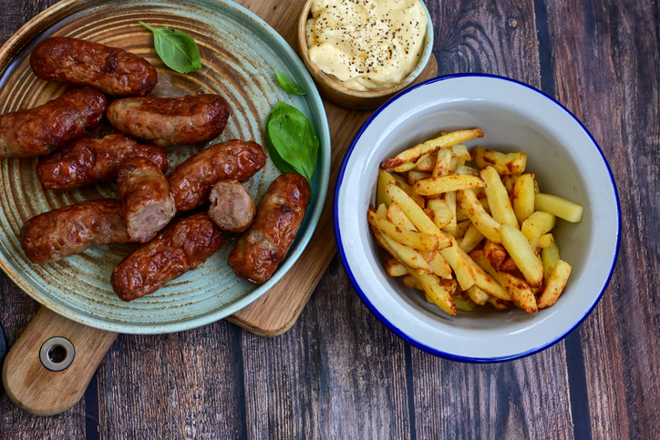 Cevapcici auf einem Teller mit Pommes frites und einem cremigen Dip, angerichtet auf einem dunklen Holztisch.