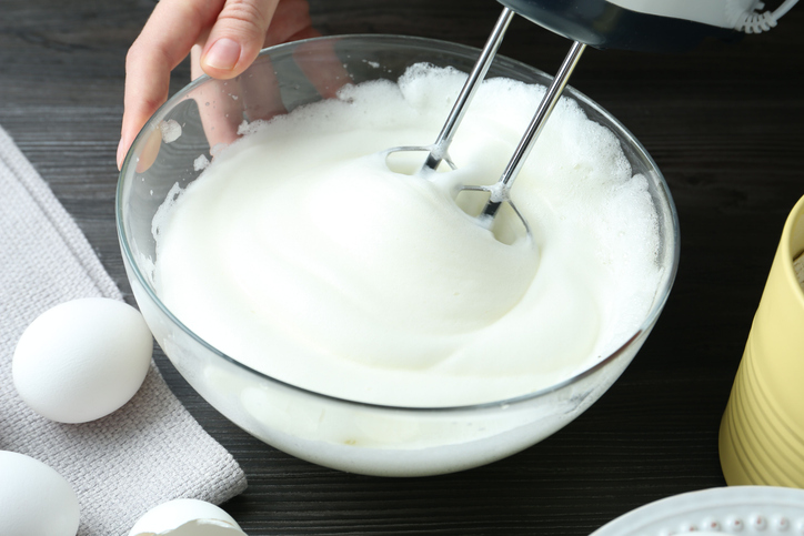 Glänzend aufgeschlagener Eischnee für Baiser in einer Glasschüssel, der mit einem Handmixer aufgeschlagen wird.