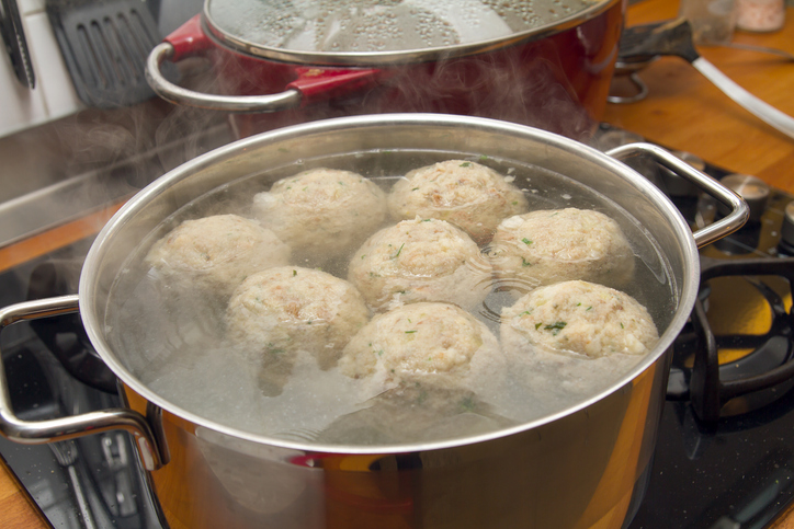 Mehrere Semmelknödel garen in einem großen Topf mit heißem Wasser auf dem Herd.