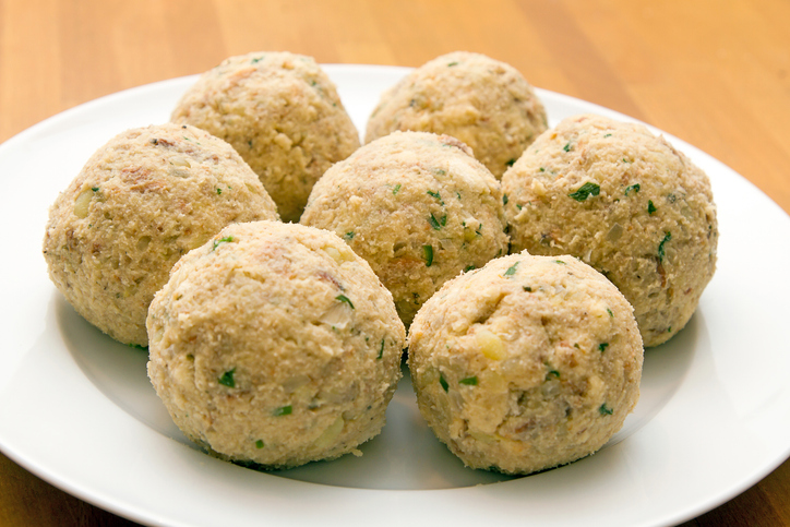 Sechs runde Semmelknödel liegen auf einem weißen Teller auf einem hellen Holztisch.