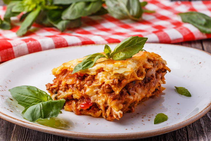 Stück Lasagne mit Hackfleischsoße, Tomaten, cremiger Béchamelsauce und geschmolzenem Käse auf einem weißen Teller.