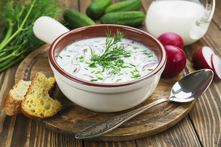 Kalte Tarator-Sauermilchsuppe in einer Schale mit Gurkenstückchen, Radieschen, Schnittlauch und frischem Dill, dazu Brot und Gemüse.