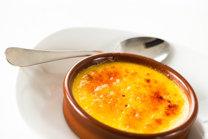 Crema Catalana in einer braunen Schale mit glänzender Zuckerkruste und zwei Löffeln auf hellem Hintergrund