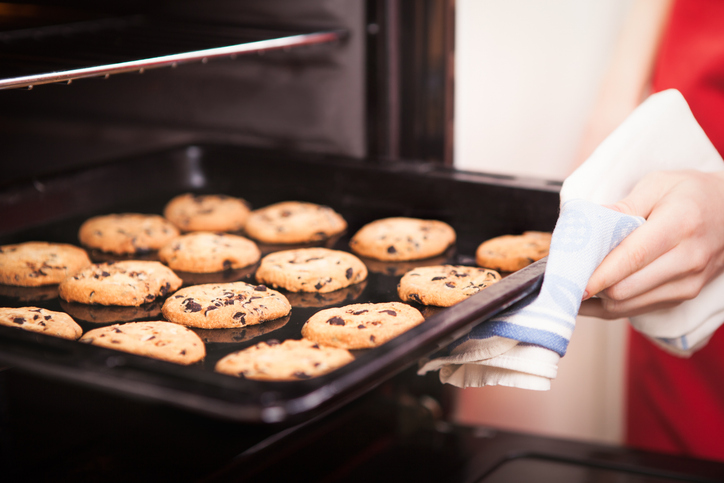 Frisch gebackene Schoko-Cookies auf einem Backblech, das gerade mit einem Tuch aus dem Ofen gezogen wird.