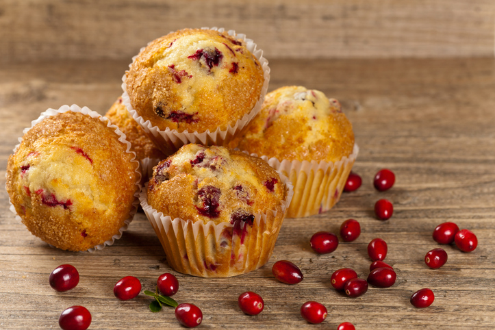 Goldbraun gebackene Cranberry Muffins mit sichtbaren roten Cranberries in Papierförmchen auf einem rustikalen Holztisch.