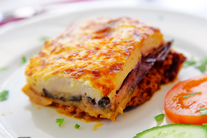 Einzelnes Stück Moussaka mit Auberginen, Hackfleischsoße und dicker goldbrauner Béchamelschicht auf einem Teller