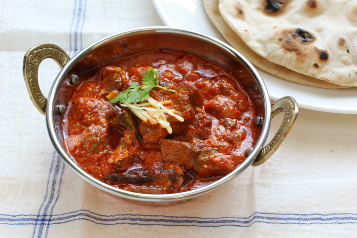 Rogan Josh mit Fleischstücken in kräftiger roter Currysoße, garniert mit Ingwerstreifen und Koriander, dazu frisches Naan-Brot.