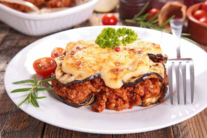 Portion Moussaka mit Auberginenscheiben, würziger Hackfleischsoße und geschmolzenem Käse auf einem weißen Teller