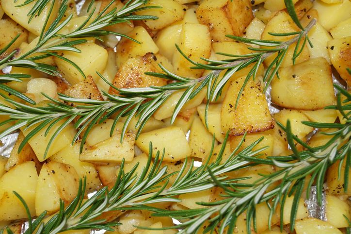 Goldene Rosmarinkartoffeln auf einem Backblech, belegt mit mehreren frischen Rosmarinzweigen.
