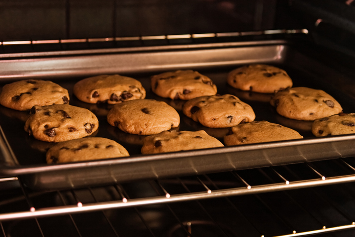 Mehrere Schoko-Cookies backen auf einem Blech im Ofen und sind bereits leicht goldbraun.