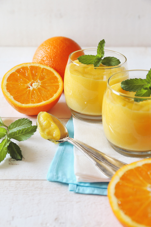 Orangenquark in zwei Gläsern mit frischen Orangen, Minzblättern und einem Löffel auf hellem Untergrund