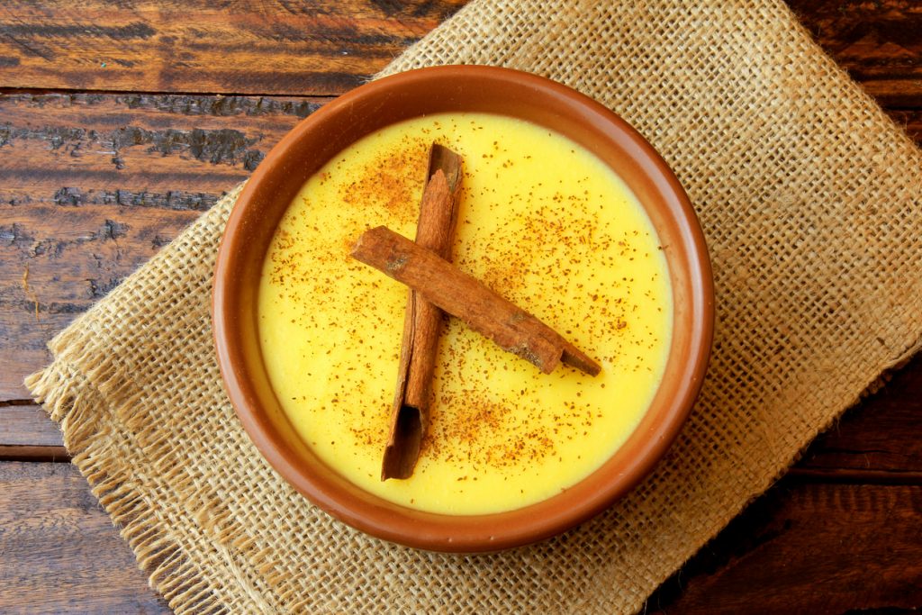 Schale mit traditionellem brasilianischem Curau, dekoriert mit Zimtstangen und Zimtpulver, serviert auf rustikalem Holztisch.