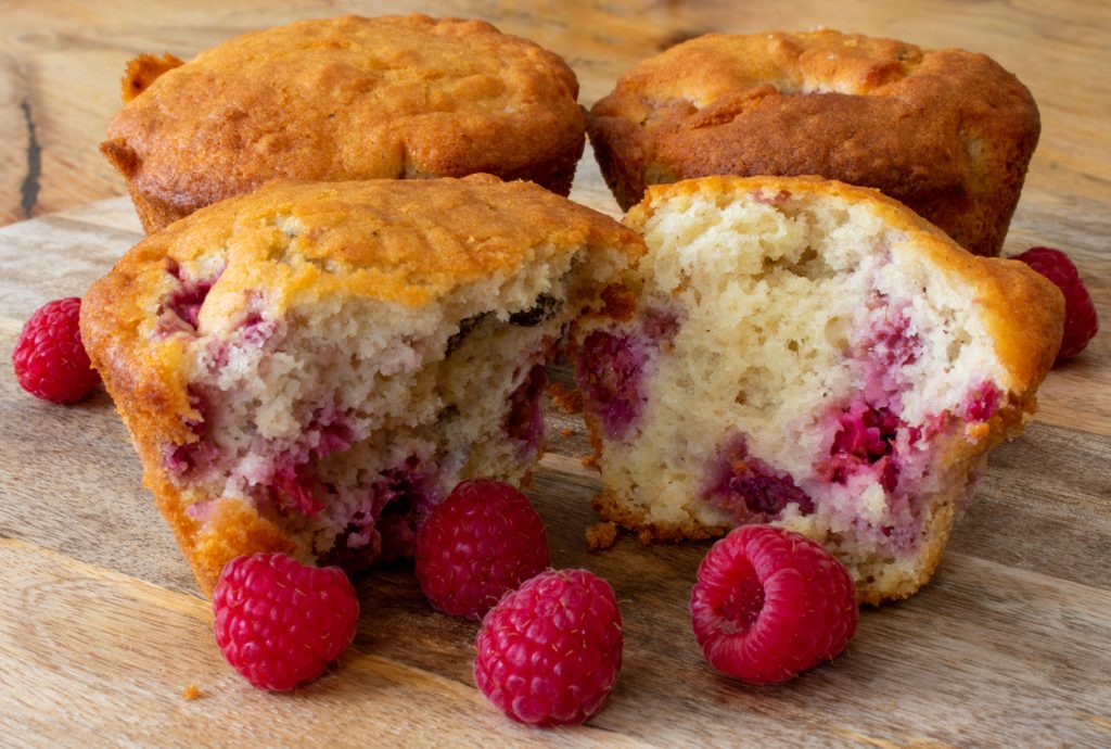 Frisch gebackene Himbeermuffins mit frischen Himbeeren auf einem Holztisch.