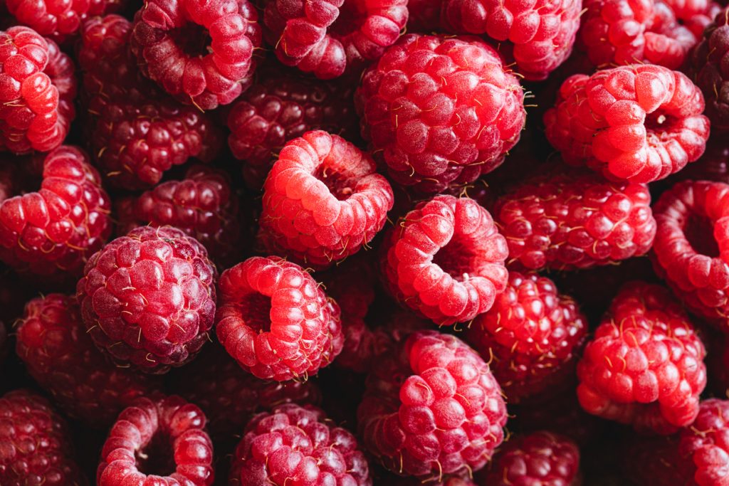 Viele reife, rote Himbeeren liegen dicht nebeneinander, fotografiert in Nahaufnahme mit sichtbarer Struktur und feinen Härchen.