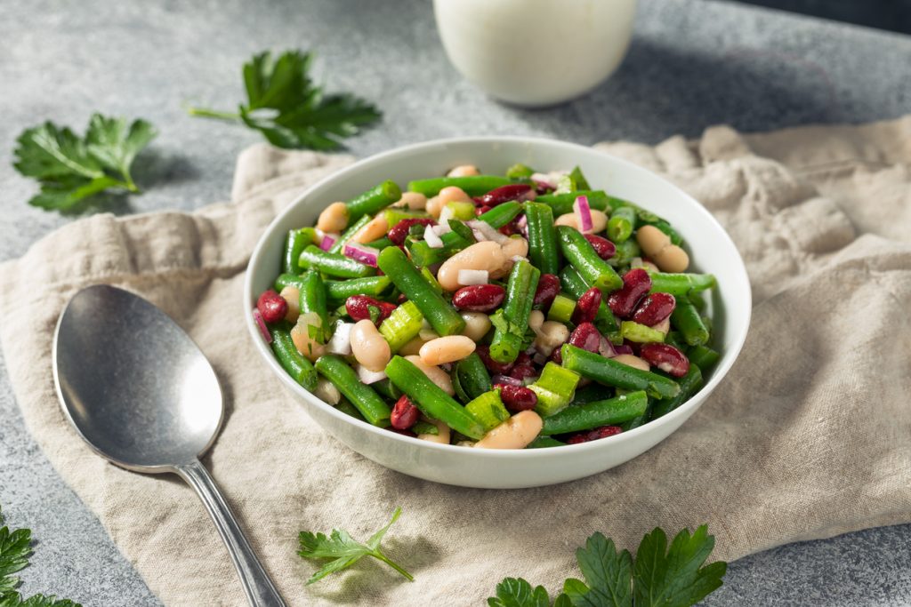 Frischer Drei-Bohnen-Salat mit grünen Bohnen, Kidneybohnen, weißen Bohnen, Zwiebeln und Petersilie in einer Schüssel.