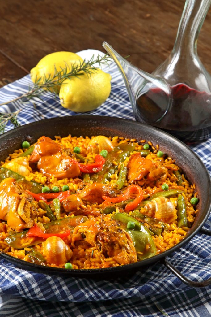 Authentische Paella Valenciana mit Hühnerfleisch, Paprika, Erbsen, Schnecken und Safranreis in einer Paellapfanne.