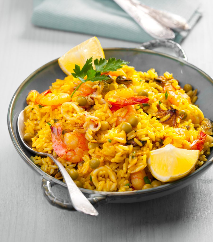 Spanische Paella mit Garnelen, Erbsen, Reis und Zitronenspalten in einer Pfanne serviert.