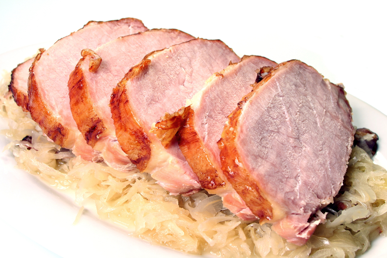 Aufgeschnittenes Kassler mit goldbrauner Kruste, serviert auf Sauerkraut auf einem weißen Teller.