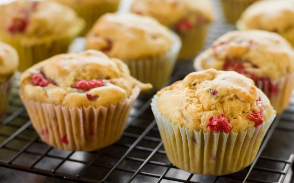 Mehrere frisch gebackene Himbeermuffins mit roten Beeren auf einem Abkühlgitter.