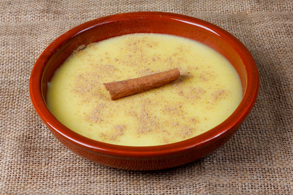 Schale mit brasilianischem Maispudding Curau, bestreut mit Zimt und dekoriert mit einer Zimtstange.