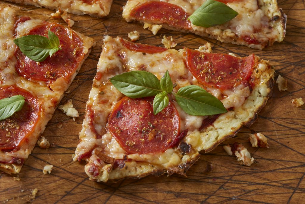Ein Stück Salamipizza mit geschmolzenem Käse, Peperoni-Salami und frischem Basilikum auf einem Holzbrett.