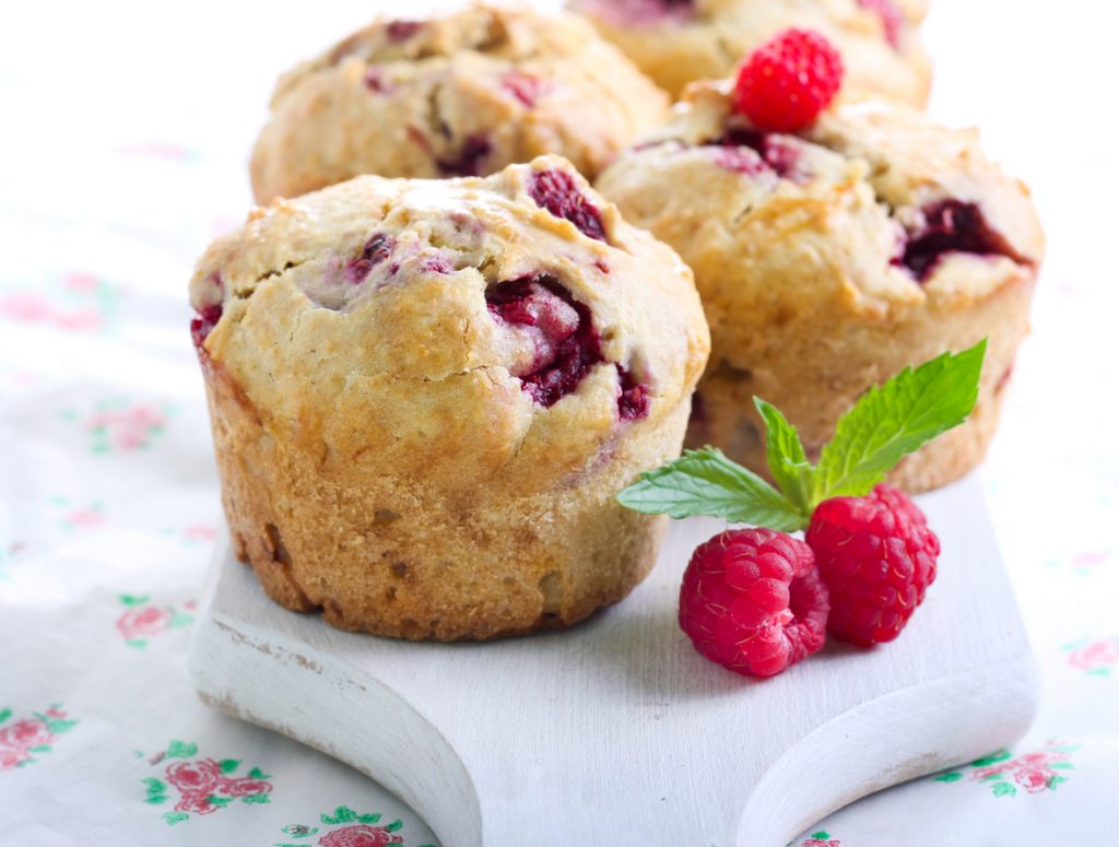 Saftige Himbeermuffins mit frischen Himbeeren und Minze auf einem weißen Holzbrett.