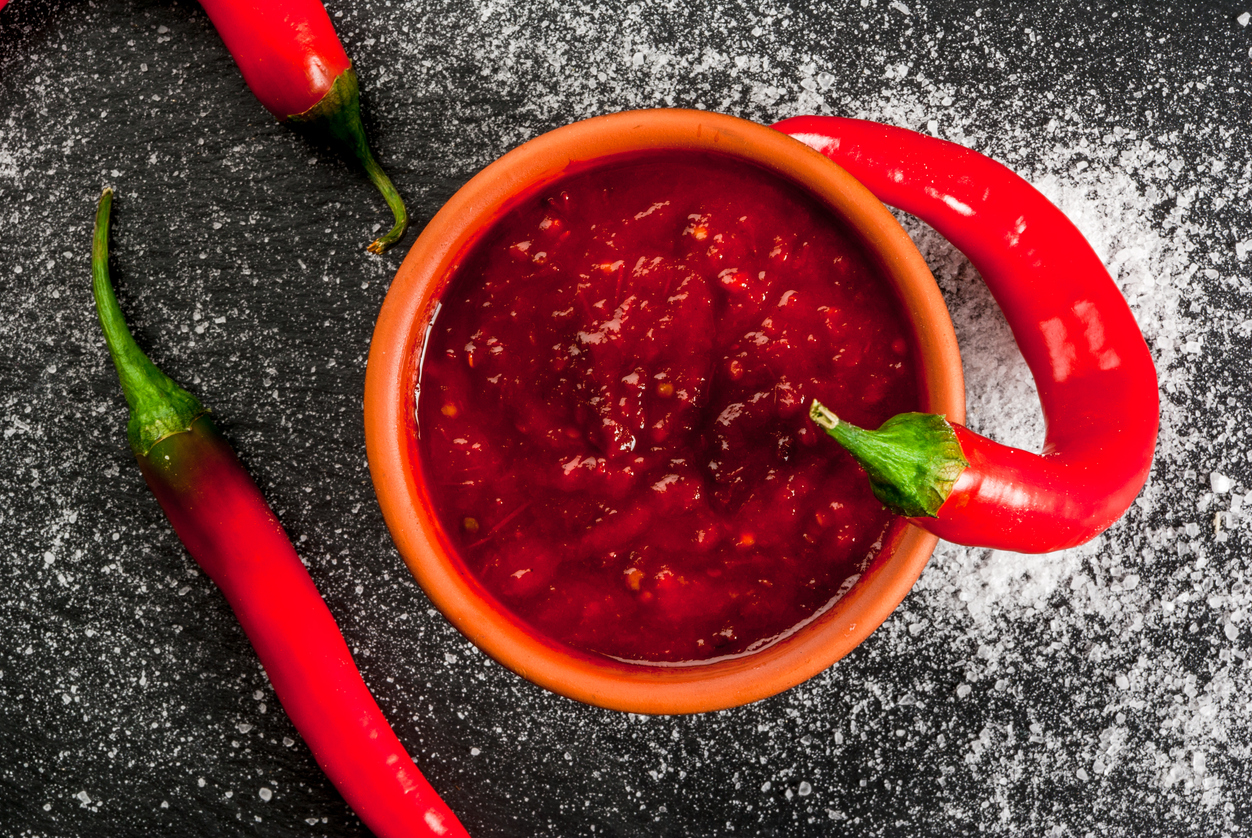 Schale mit feuriger Tabasco-Sauce, dekoriert mit frischen roten Chilischoten auf schwarzem Untergrund.