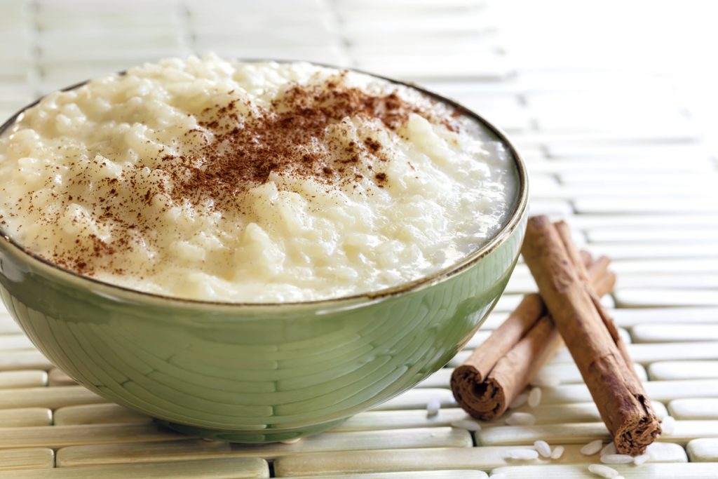 Schüssel mit cremigem Milchreis, bestreut mit Zimt und Zucker, daneben Zimtstangen.