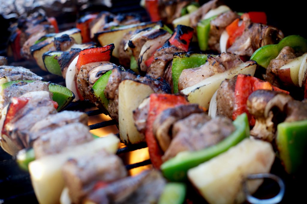 Bunte Grillspieße mit Lammfleisch, Paprika, Zwiebeln, Pilzen und Kartoffeln auf dem Grill über offener Flamme.