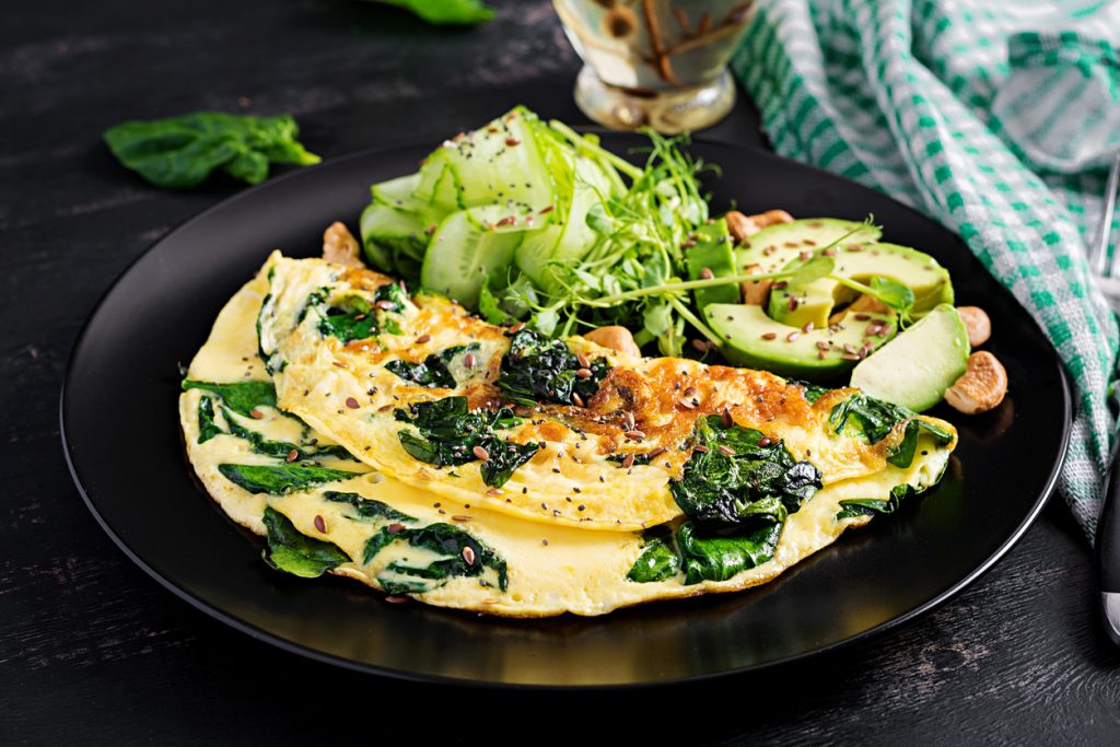 Omelett mit Spinat und Avocado mit grünem Salat auf schwarzem Teller