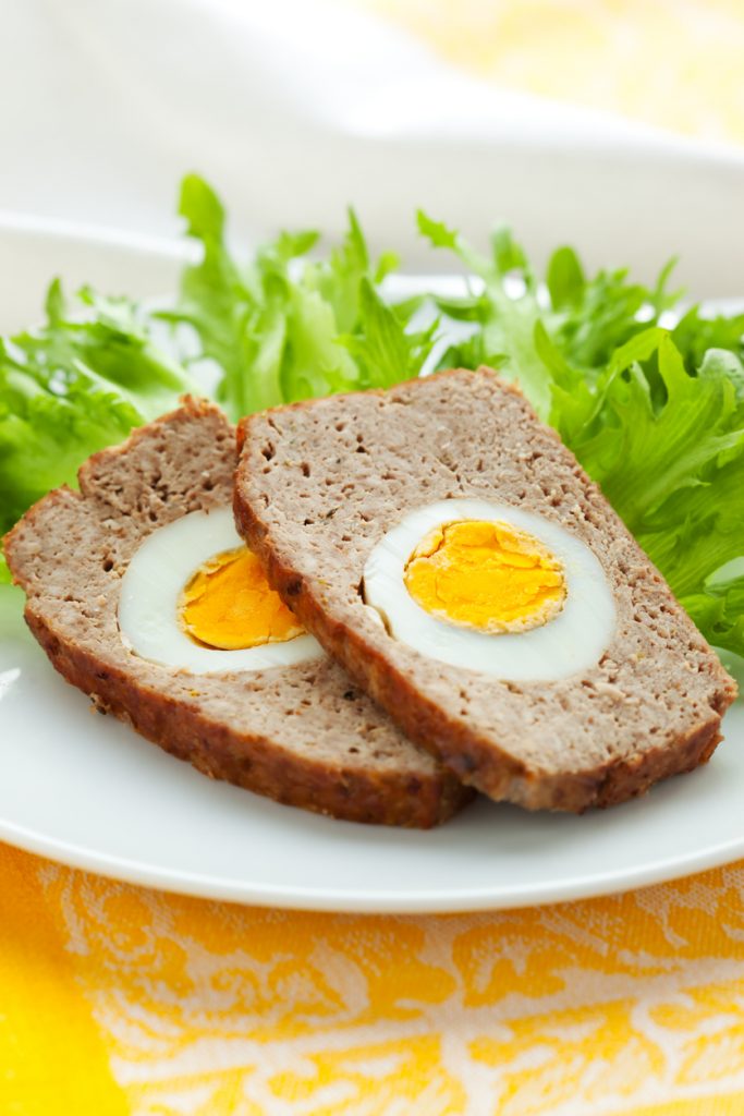 Zwei Scheiben Hackbraten mit hartgekochtem Ei in der Mitte, serviert auf einem weißen Teller mit frischem grünen Salat.