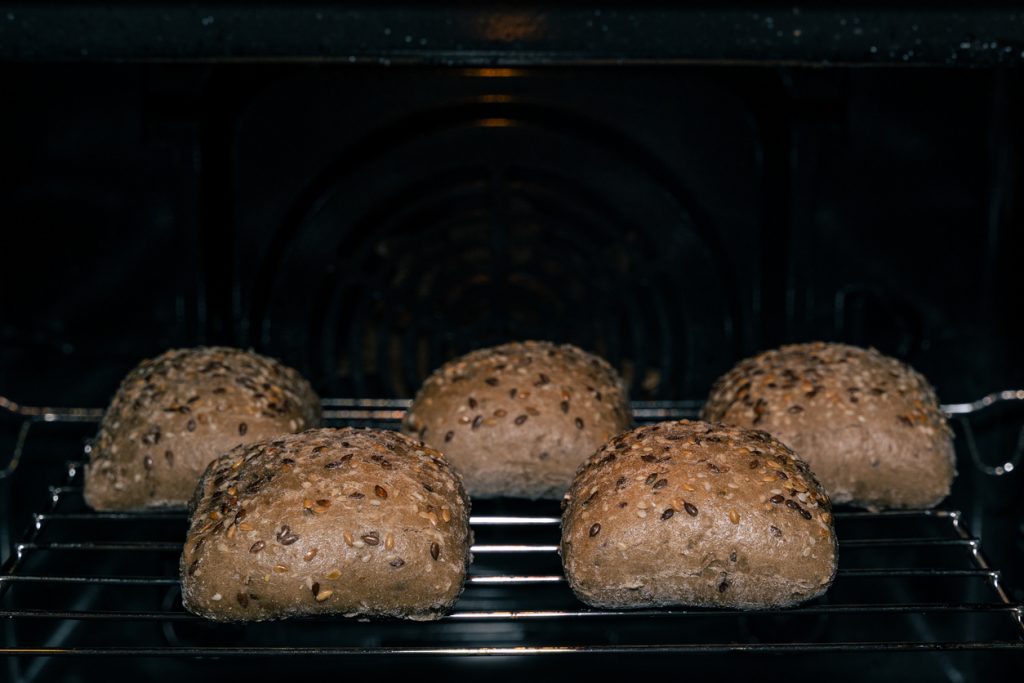 Fünf Mehrkornbrötchen mit Sesam- und Leinsamen backen auf einem Ofenrost.