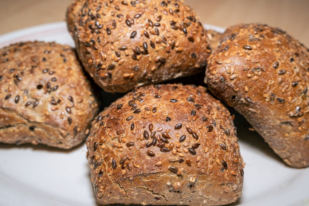 Vier goldbraune Mehrkornbrötchen mit Sesam- und Leinsamen auf einem Teller.