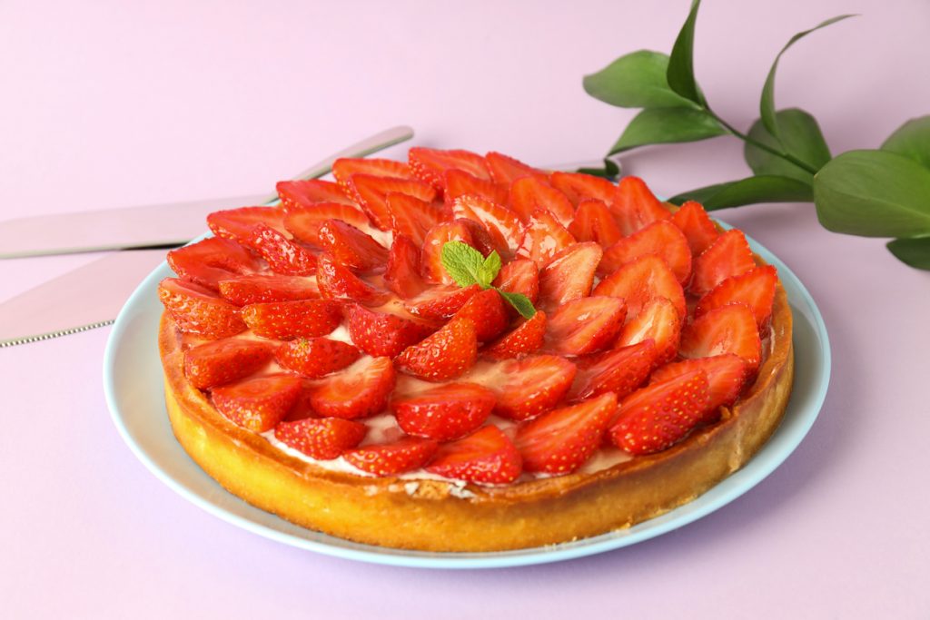 Erdbeerkuchen mit halbierten, glänzenden Erdbeeren auf Mascarponecreme, serviert auf Teller.