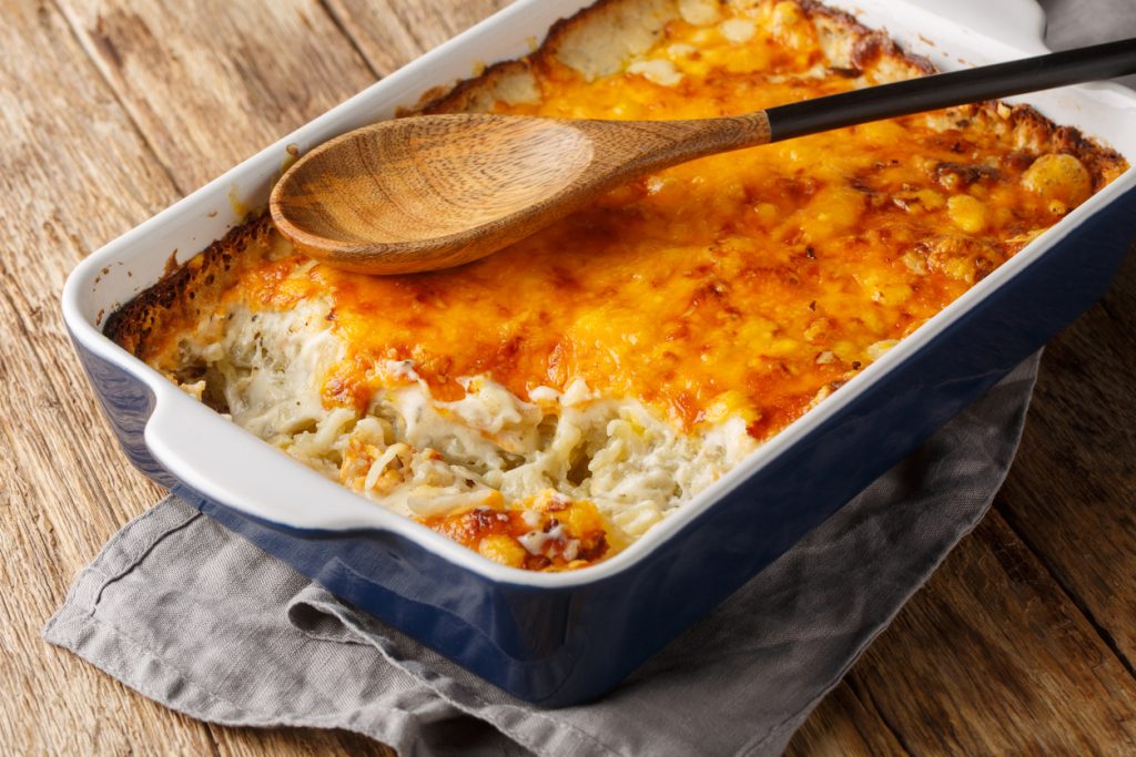 Rechteckige Auflaufform mit frisch gebackenem Käse-Rösti-Auflauf; eine entnommene Portion zeigt cremige Kartoffelraspeln unter der Kruste.