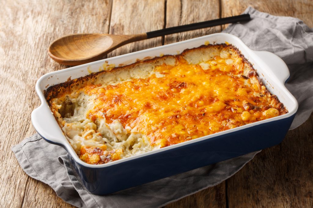 Rechteckige Auflaufform mit Käse-Rösti-Auflauf; eine entnommene Ecke zeigt cremige Kartoffelraspeln unter der goldbraunen Käsekruste.