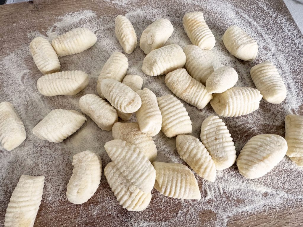 Frisch geformte Gnocchi, bemehlt und bereit zum Kochen, liegen auf einem Holzbrett.