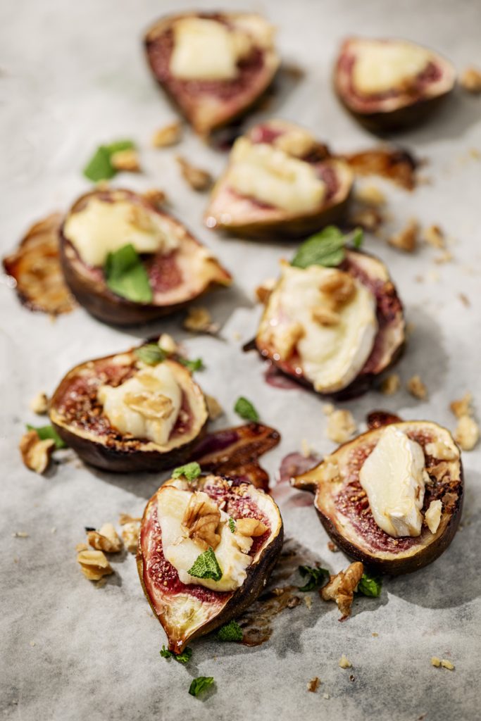 Gebackene Feigenhälften mit geschmolzenem Ziegenkäse und Walnüssen auf Backpapier, servierfertig.