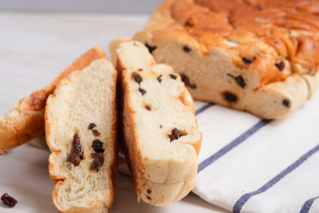Aufgeschnittenes frisches Rosinenbrot auf einem gestreiften Küchentuch, im Hintergrund der restliche Laib.