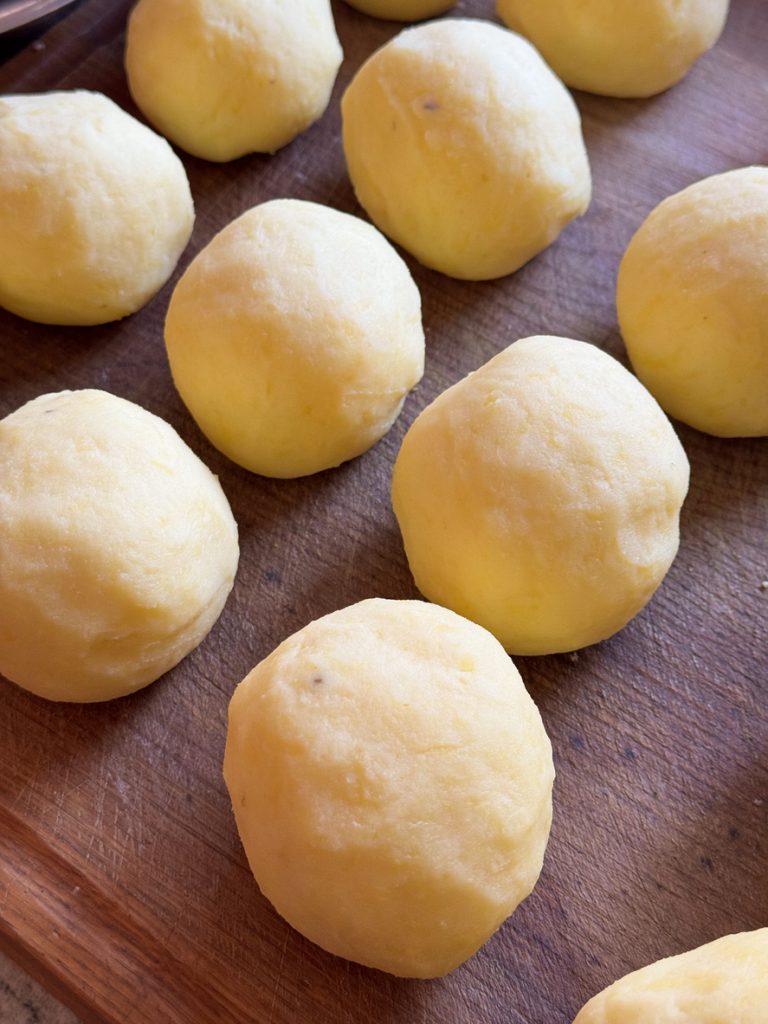 Mehrere handgedrehte Kartoffelklöße auf einem Holzbrett, roh und noch ungekocht.