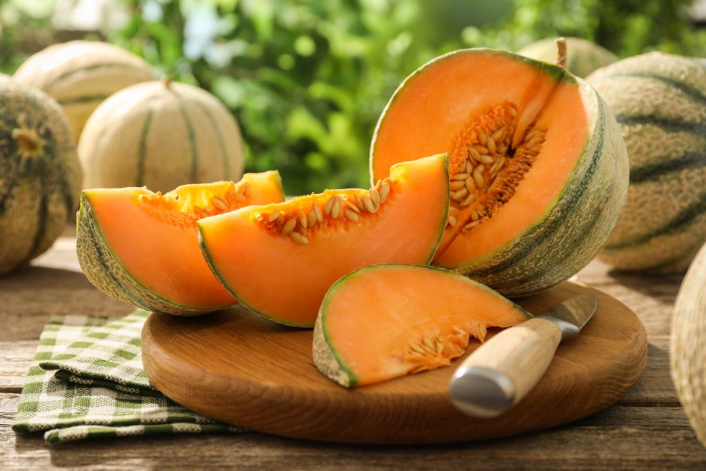 Aufgeschnittene Cantaloupe mit orangefarbenem Fruchtfleisch und Kernen, angerichtet auf einem Holzbrett mit Messer.