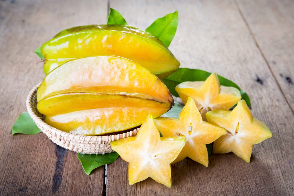 Aufgeschnittene Sternfrucht zeigt die typische sternförmige Form, daneben ganze Früchte in einem Korb auf einem Holztisch.