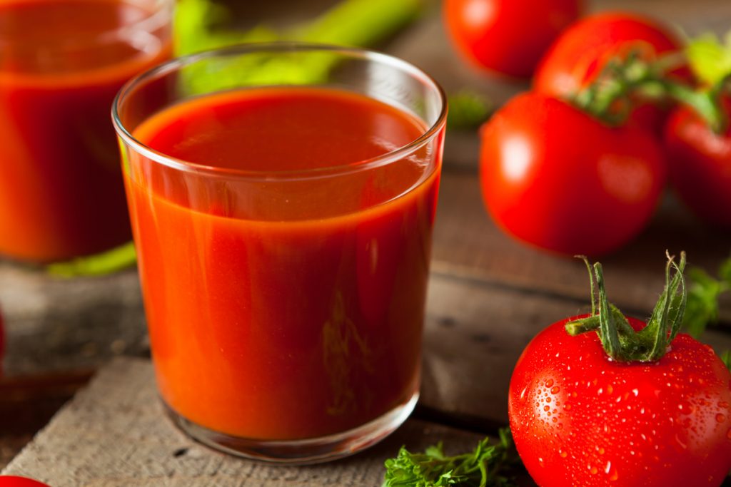 Glas mit Tomatensaft auf rustikalem Holztisch, daneben frische rote Tomaten mit Wassertropfen und Kräutern.