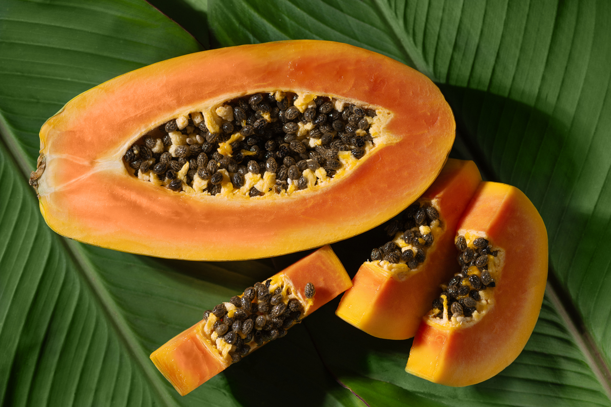 Halbierte reife Papaya mit schwarzen Kernen und mehrere Papayaspalten auf grünen Bananenblättern.