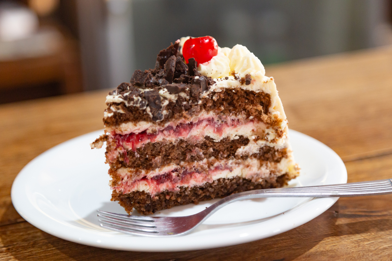Ein Stück Schwarzwälder Kirschtorte mit Sahne, Kirschen und Schokoraspeln auf weißem Teller.