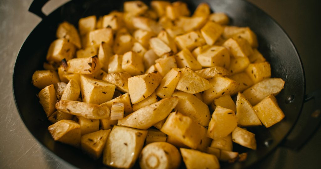 Schwarze Pfanne mit goldbraun gerösteten Pastinakenwürfeln, sichtbar gewürzt und knusprig an den Rändern.
