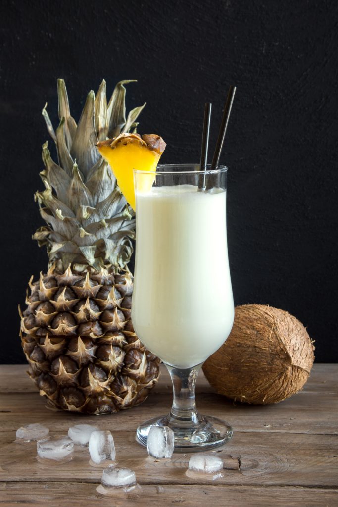 Cremiger Pina-Colada vor Ananas und Kokosnuss auf Holztisch.