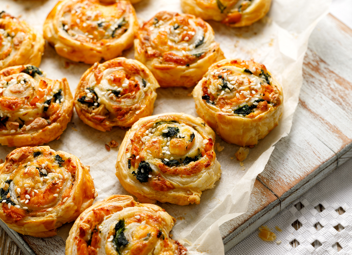 Goldbraune Blätterteig-Schnecken mit Lachs, Spinat und Käse liegen auf Backpapier.