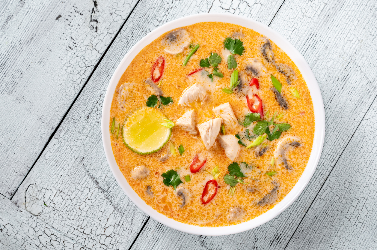 Weiße Schüssel mit Kokos-Hühnersuppe, Pilzen, Chili, Koriander und Limettenspalte.