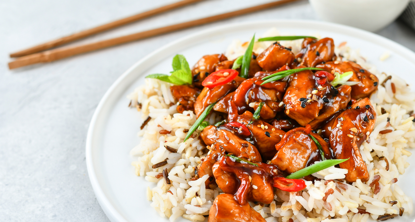 Nahaufnahme von Hühnchen in Teriyaki-Sauce mit Sesam, Chili und Frühlingszwiebeln auf Wildreis.
